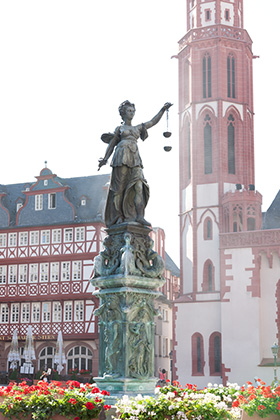 Der Brunnen mit der Justitia-Statue steht auf dem Römerberg. In ihrer Rechten hält die Bronzefigur ein Schwert, in ihrer Linken eine Waage. Unter ihr sind figürliche Reliefs angebracht.